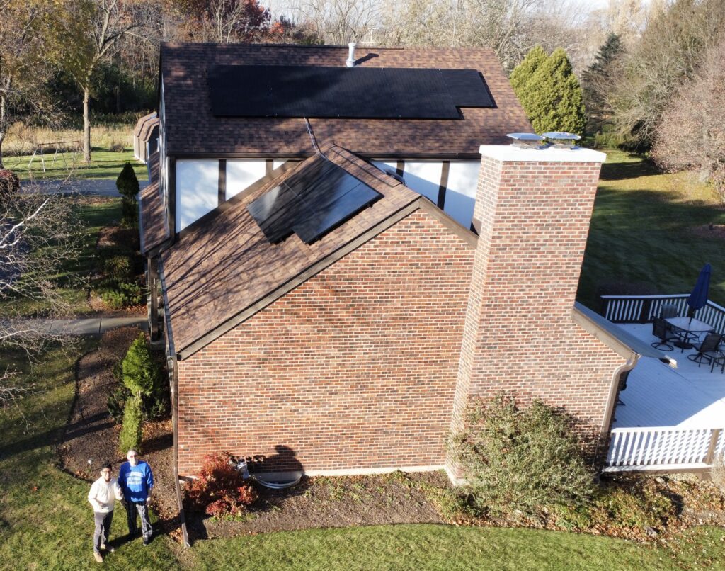 Aerial view of a brick Illinois home with newly installed rooftop solar panels, with two homeowners standing outside in the yard.