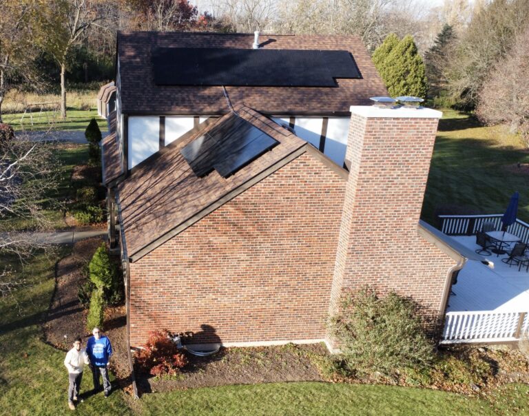 Aerial view of a brick Illinois home with newly installed rooftop solar panels, with two homeowners standing outside in the yard.