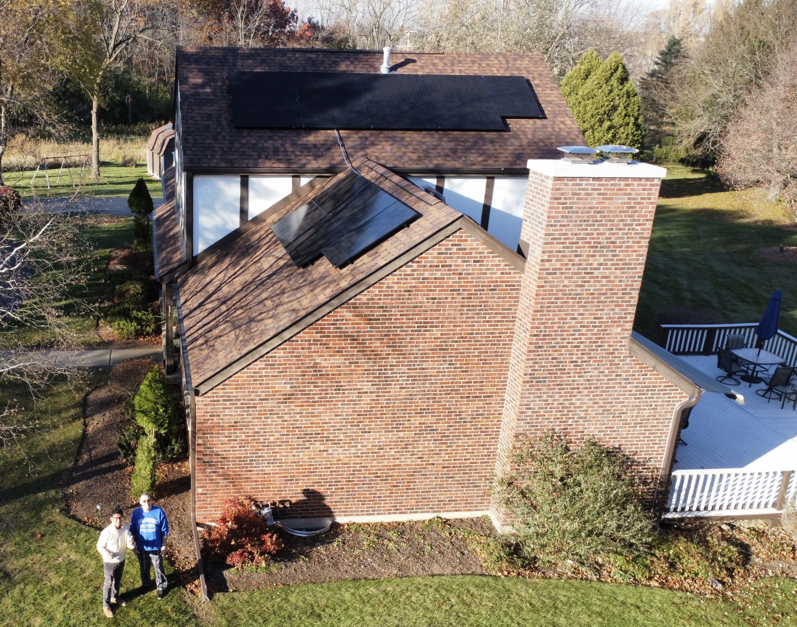Aerial view of a brick Illinois home with newly installed rooftop solar panels, with two homeowners standing outside in the yard.