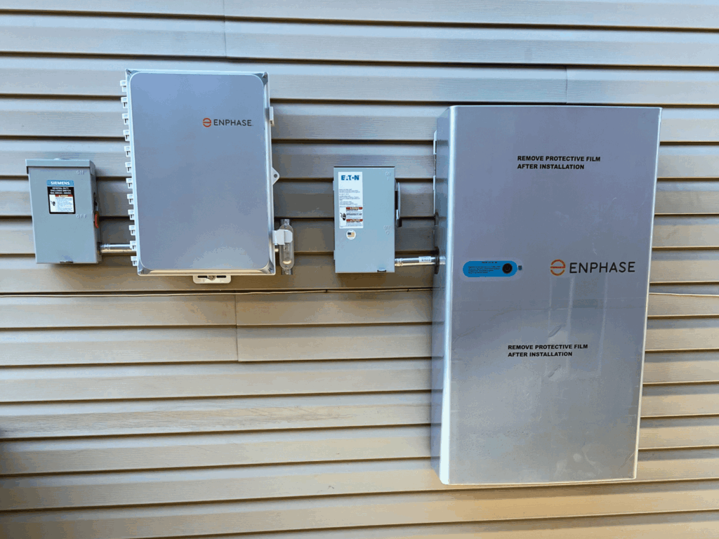 Enphase home battery storage system installed on exterior wall with electrical panel connections