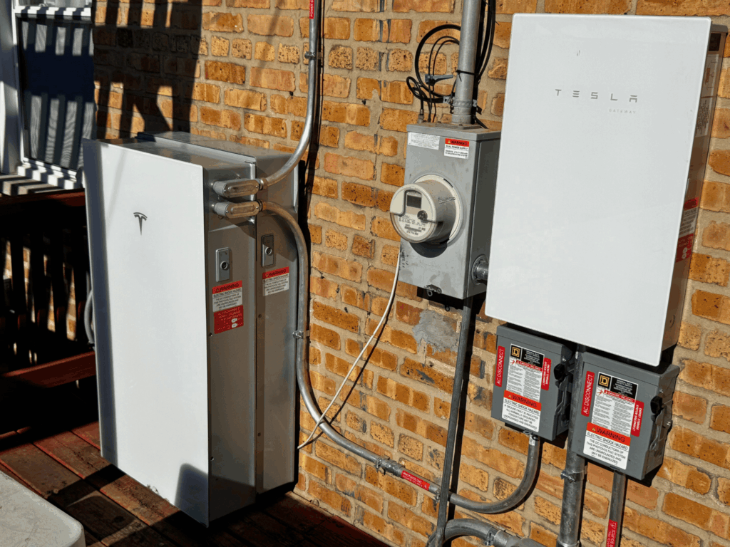 Tesla Powerwall home battery storage system installed next to electrical panel on brick exterior wall